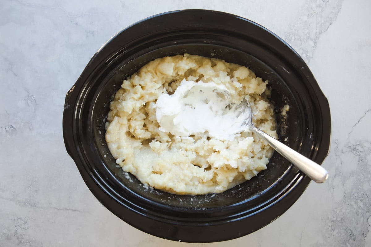 A crockpot full of mashed potatoes with sour cream.