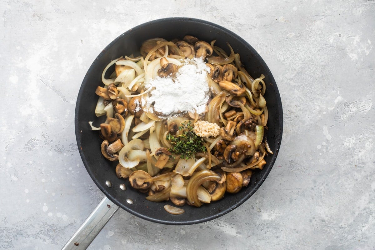 Steak tips with mushroom gravy ingredients cooking in a black skillet.