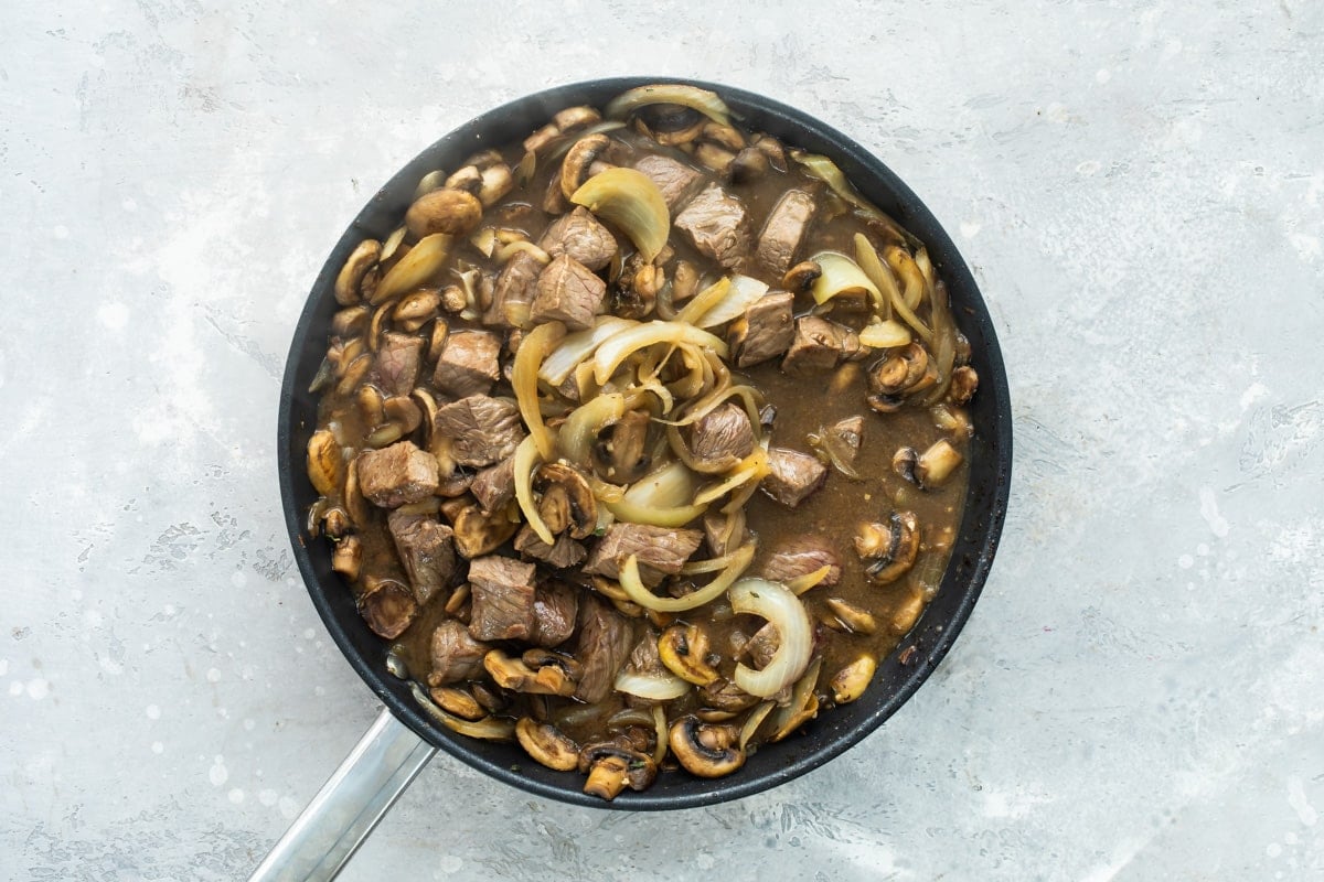 Steak tips with mushroom gravy in a black skillet.