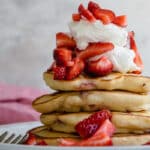 A stack of strawberry pancakes topped with whipped cream strawberries.
