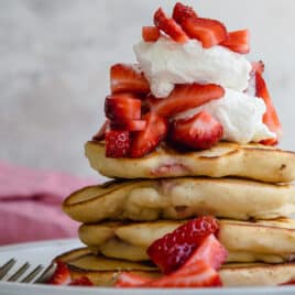 A stack of strawberry pancakes topped with whipped cream strawberries.