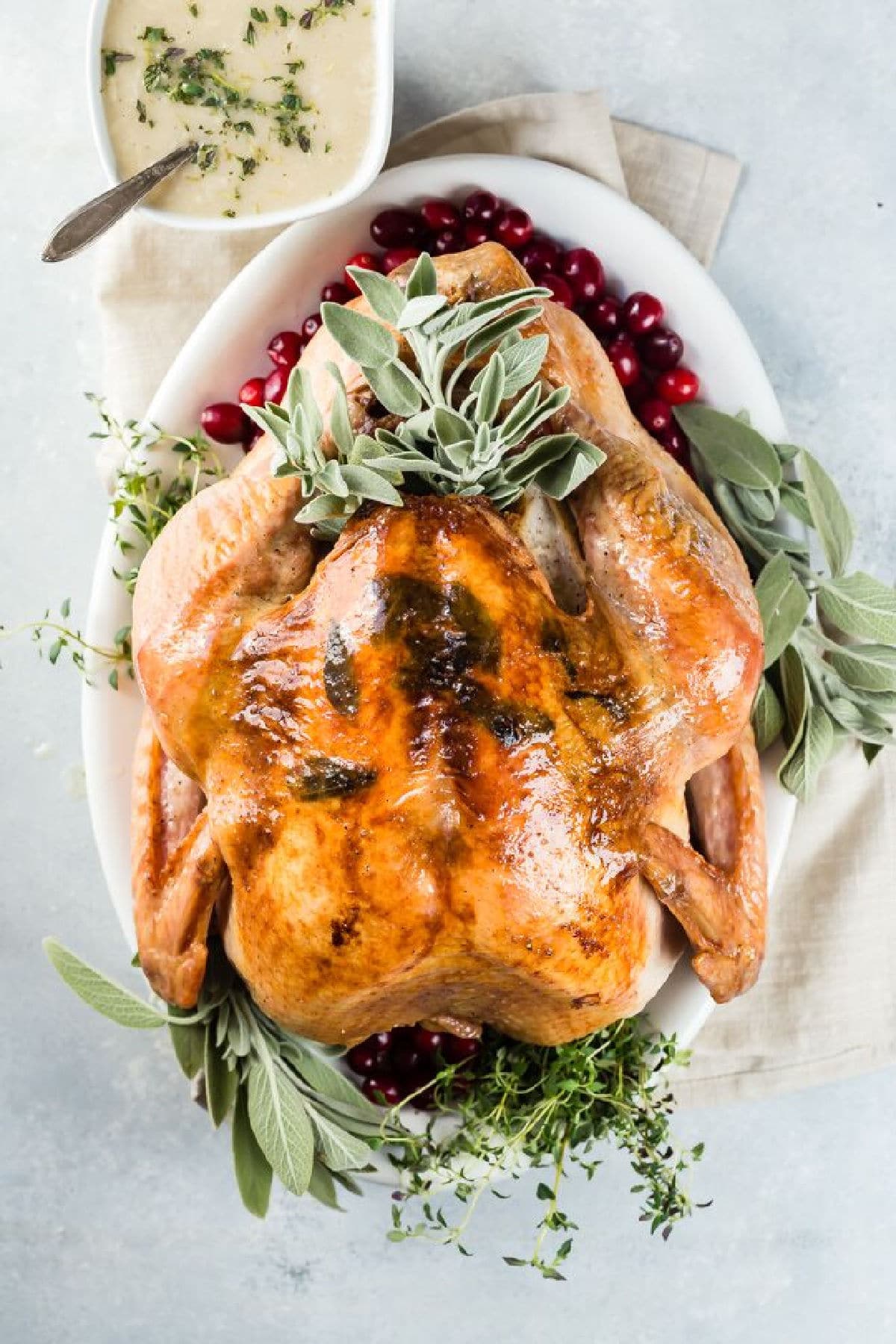 A roasted turkey on a platter with fresh herbs and cranberries.