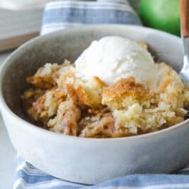 A serving of apple cobbler in a gray bowl topped with ice cream.