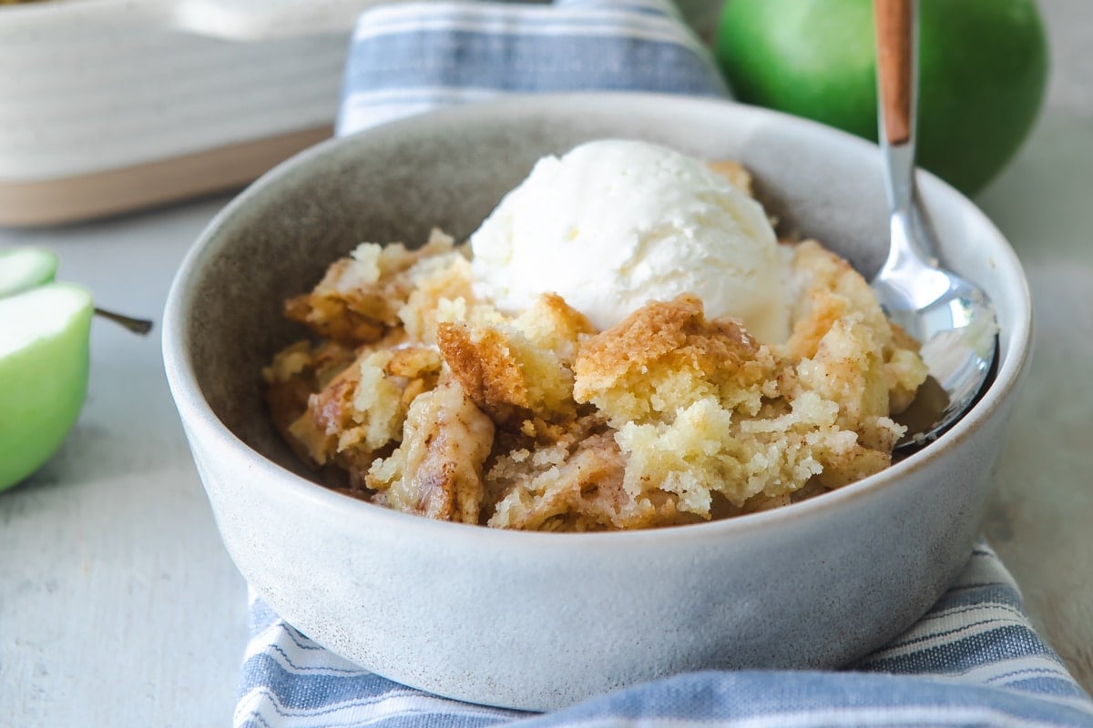 A serving of apple cobbler in a gray bowl topped with ice cream.