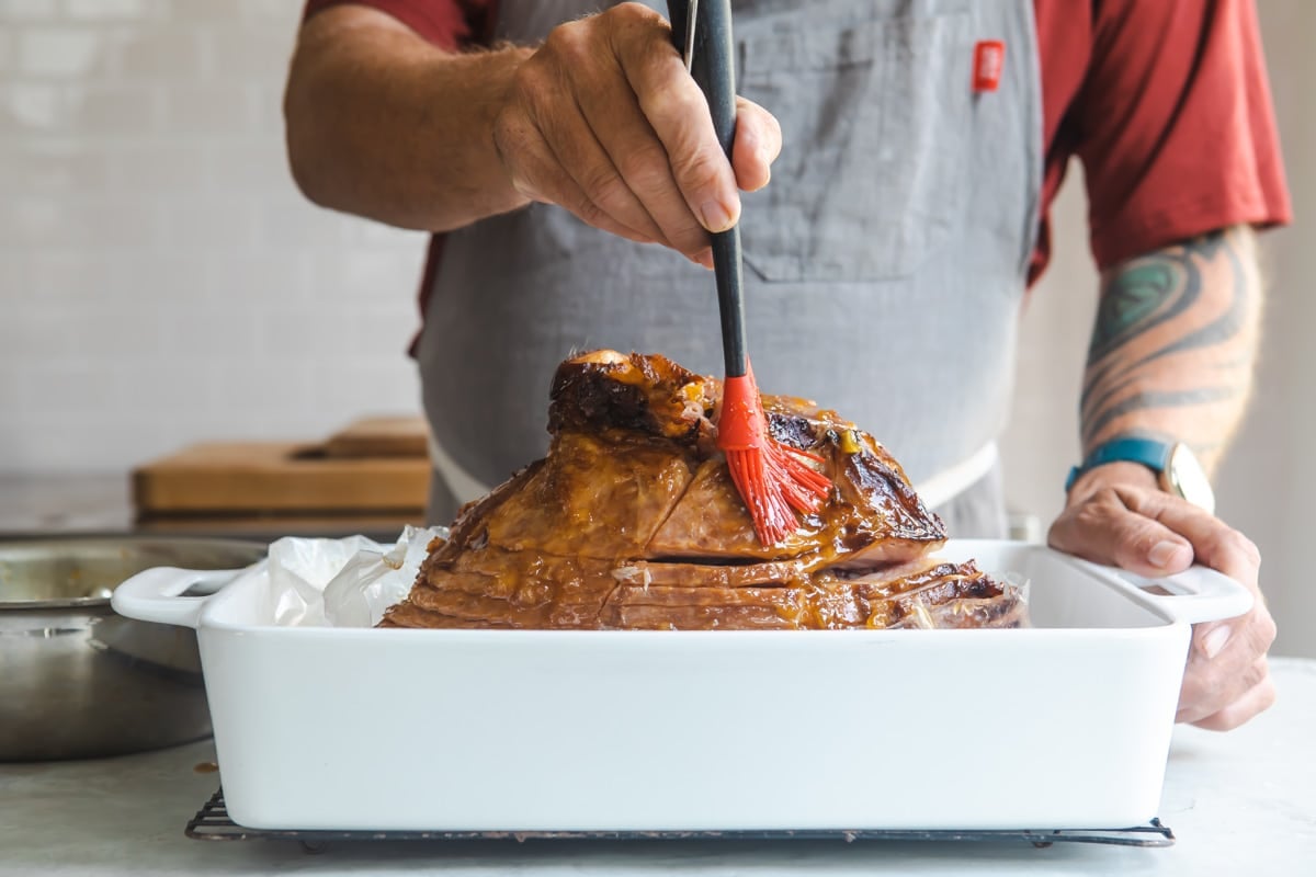 Brushing glaze on a ham in a baking dish.