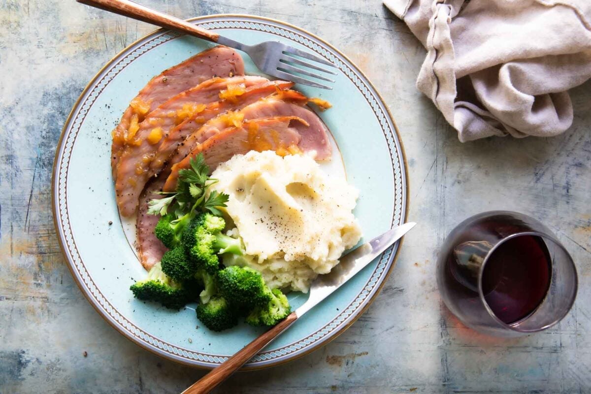 A plate of glazed ham, mashed potatoes, and broccoli.