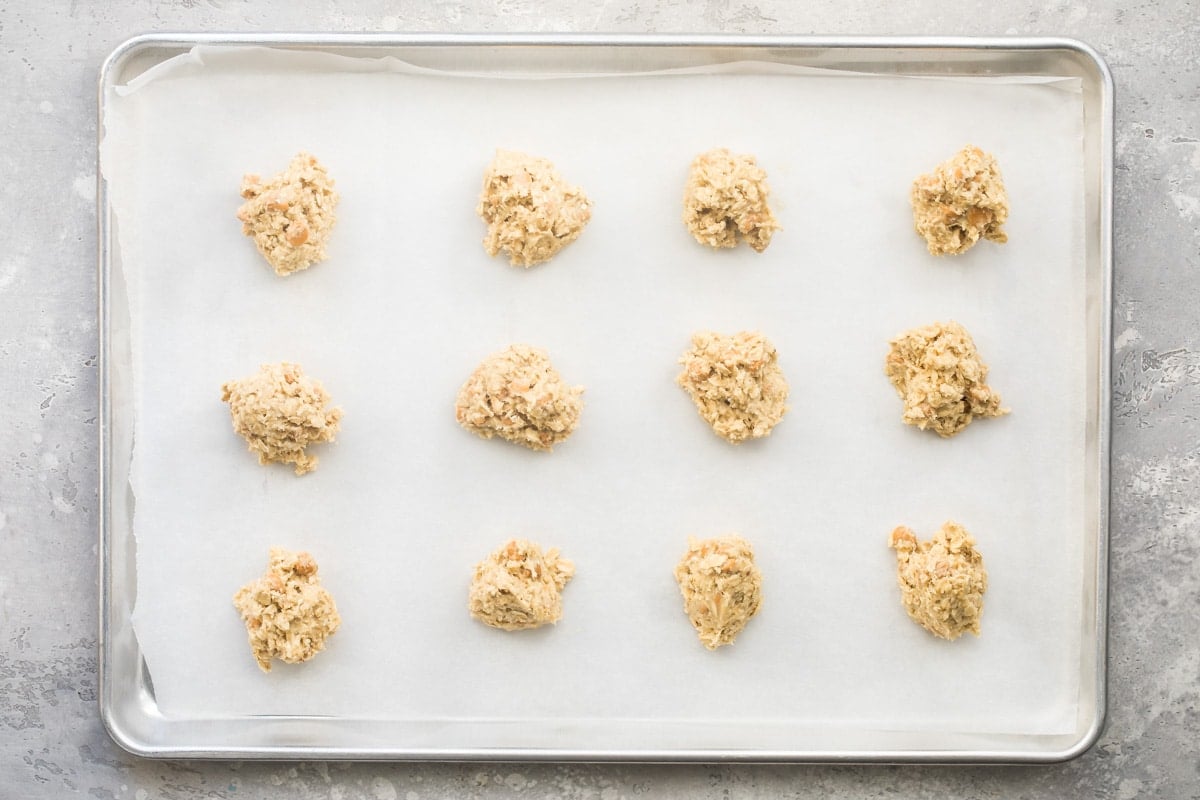 Uncooked oatmeal scotchie dough rolled into balls on a silver baking sheet.