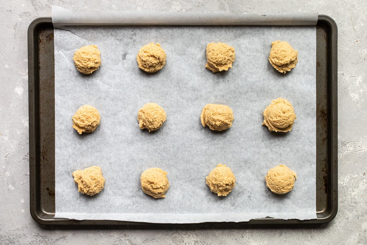 Twelve balls of peanut butter cookie dough on a baking sheet lined with parchment paper.