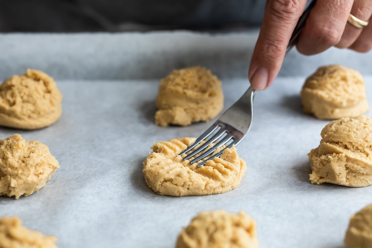 Someone pressing the cookie dough flat with a fork.
