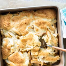 A pear cobbler in a square pan with a spoon resting in it.