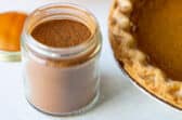 A jar of pumpkin pie spice next to a pumpkin pie.