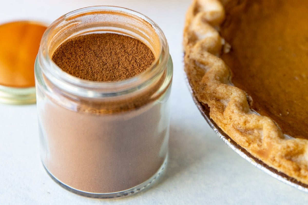 A jar of pumpkin pie spice next to a pumpkin pie.
