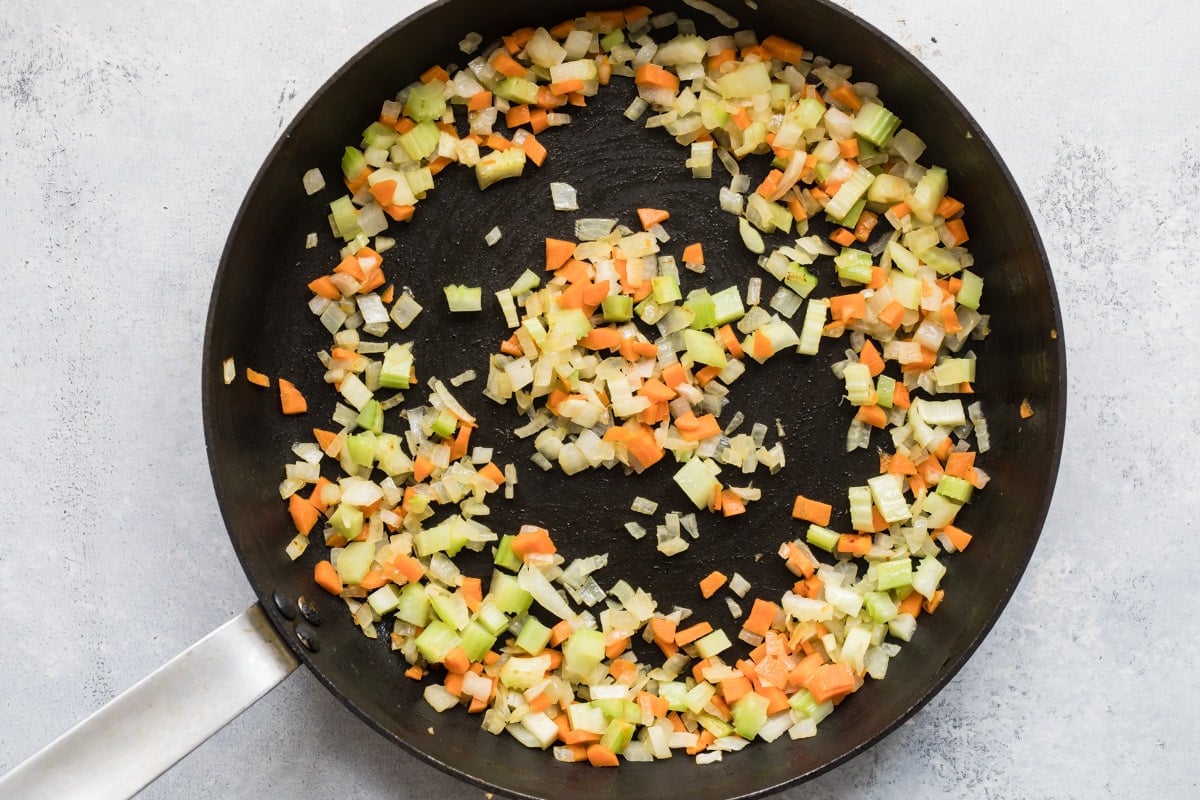 Onion, celery and carrots being cooked in a skilllet.