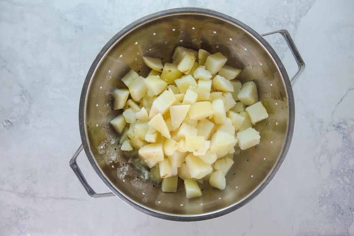 Cubed potatoes draining in a strainer.