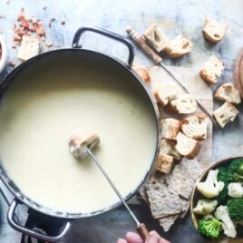 A piece of bread being dipped in cheese fondue.
