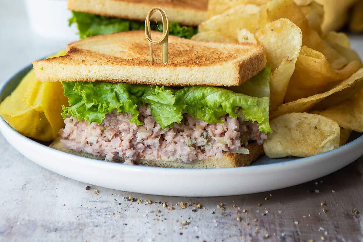 A ham salad sandwich on toast next to chips and a pickle.