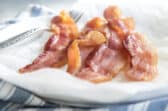 Slices of cooked bacon on paper towels on a white plate.
