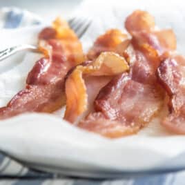 Slices of cooked bacon on paper towels on a white plate.