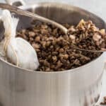 Cooked lentils in a silver pot with some in a spoon resting on the edge of the pot.