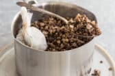 Cooked lentils in a silver pot with some in a spoon resting on the edge of the pot.
