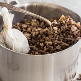 Cooked lentils in a silver pot with some in a spoon resting on the edge of the pot.