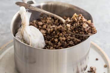 Cooked lentils in a silver pot with some in a spoon resting on the edge of the pot.