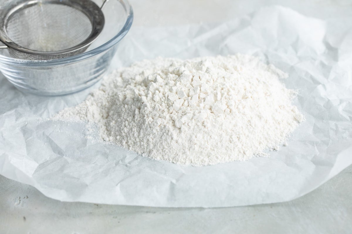 Sifted flour on parchment paper with a flour sifter next to it.