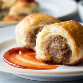 Two sausage rolls on a plate with a swirl of ketchup.