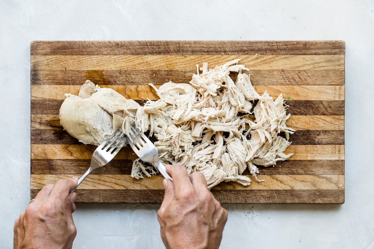 Someone pulling chicken on a wood cutting board.