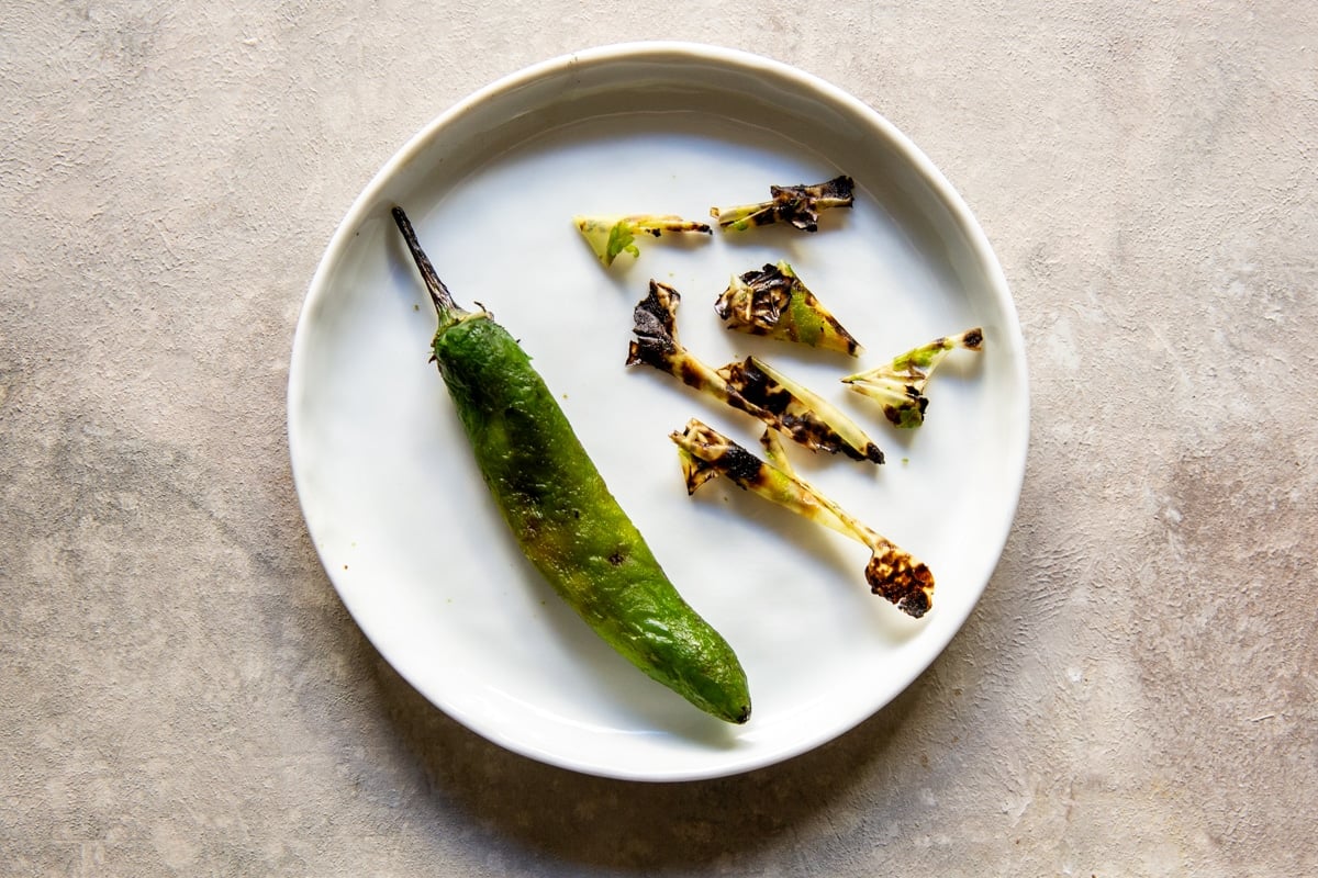 A peeled roasted serrano pepper on a white plate.
