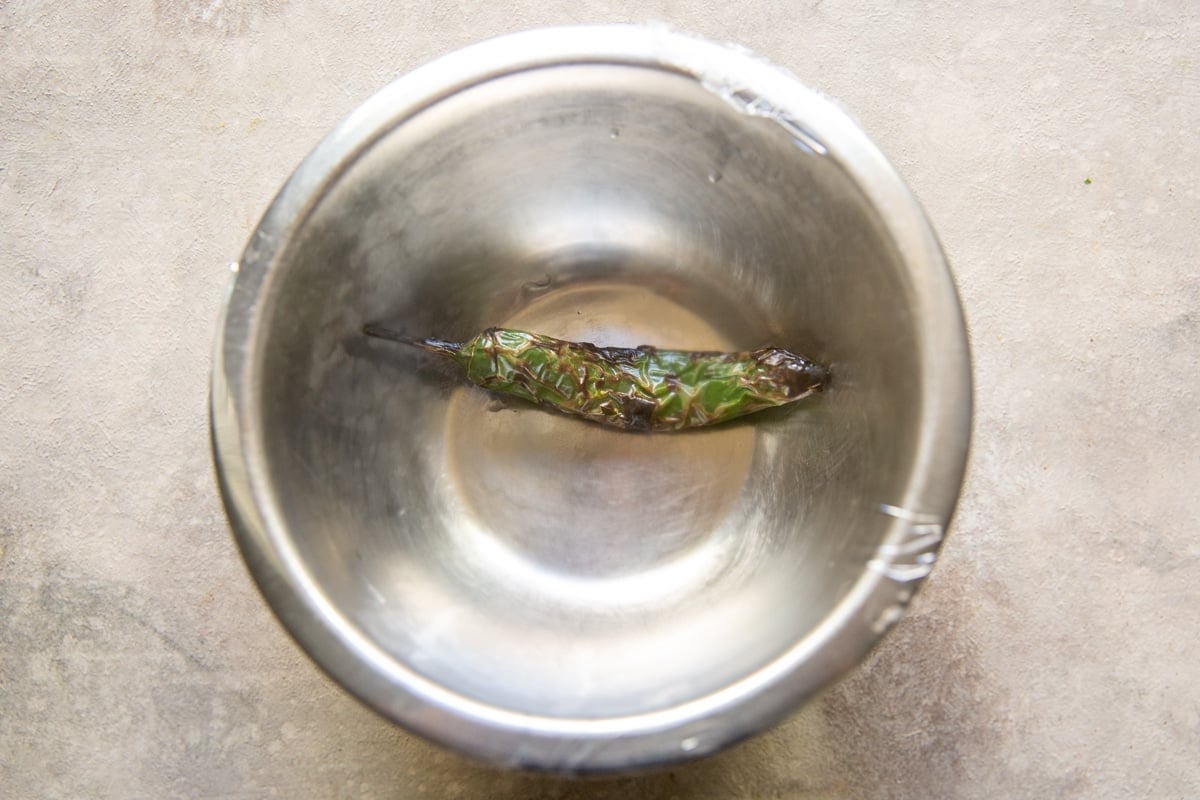 A roasted serrano pepper in a bowl covered with plastic wrap.