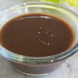 Balsamic Vinaigrette in a clear glass dish next to leafs of romaine lettuce.