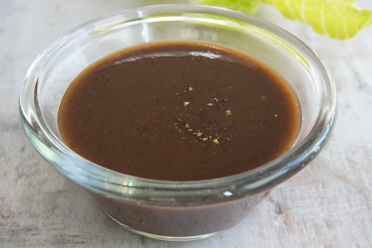 Balsamic Vinaigrette in a clear glass dish next to leafs of romaine lettuce.