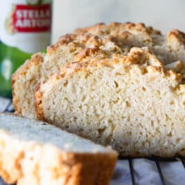 A loaf of beer bread cut into slices on a cooling rack.