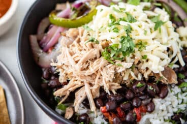 A burrito bowl filled with Chipotle copycat Carnitas, white rice, black beans, salsa, and fajita veggies.