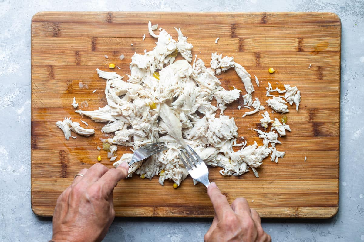 Someone shredding chicken on a wooden cutting board.