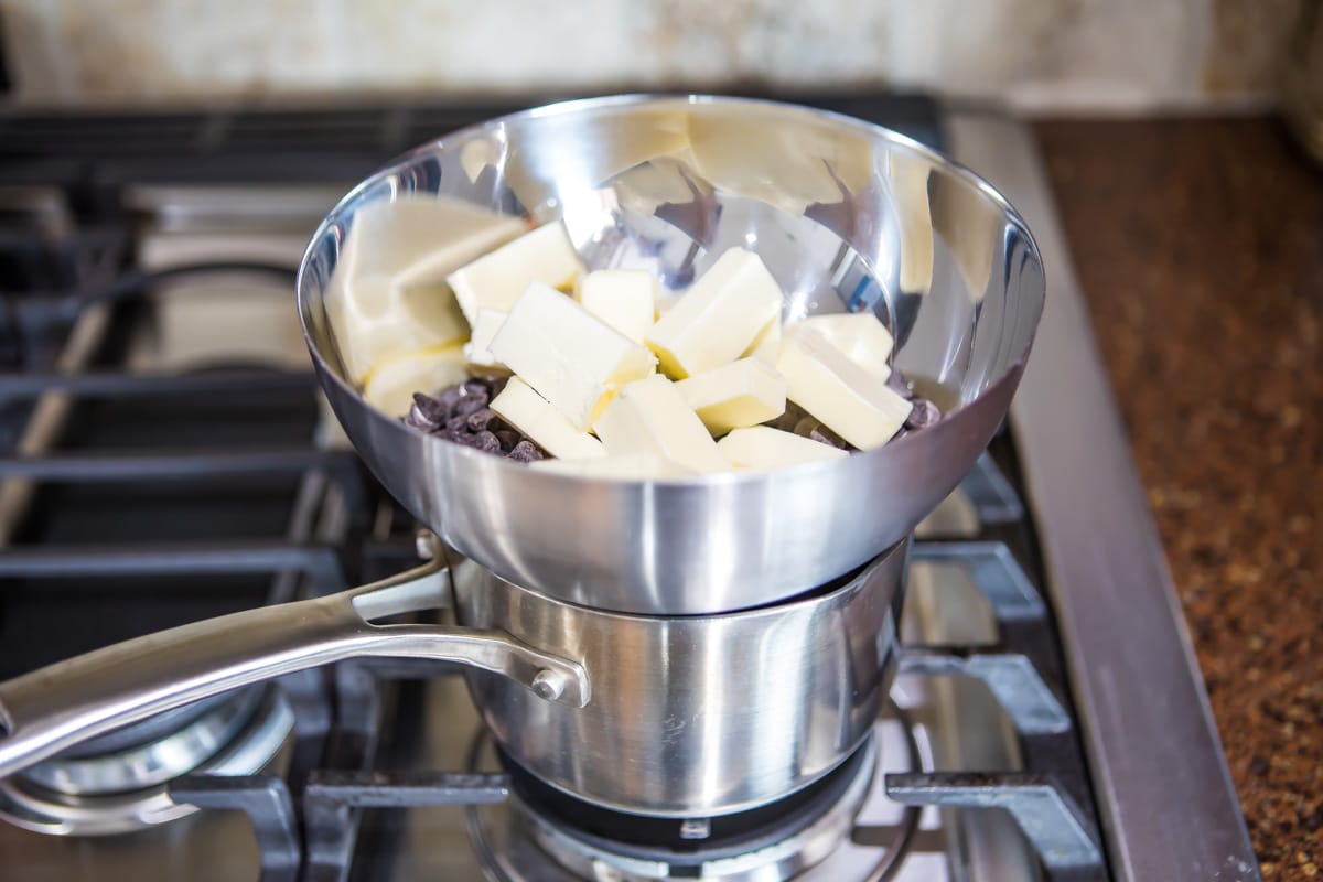 Chocolate chips and butter in a silver bowl on top of a pot.