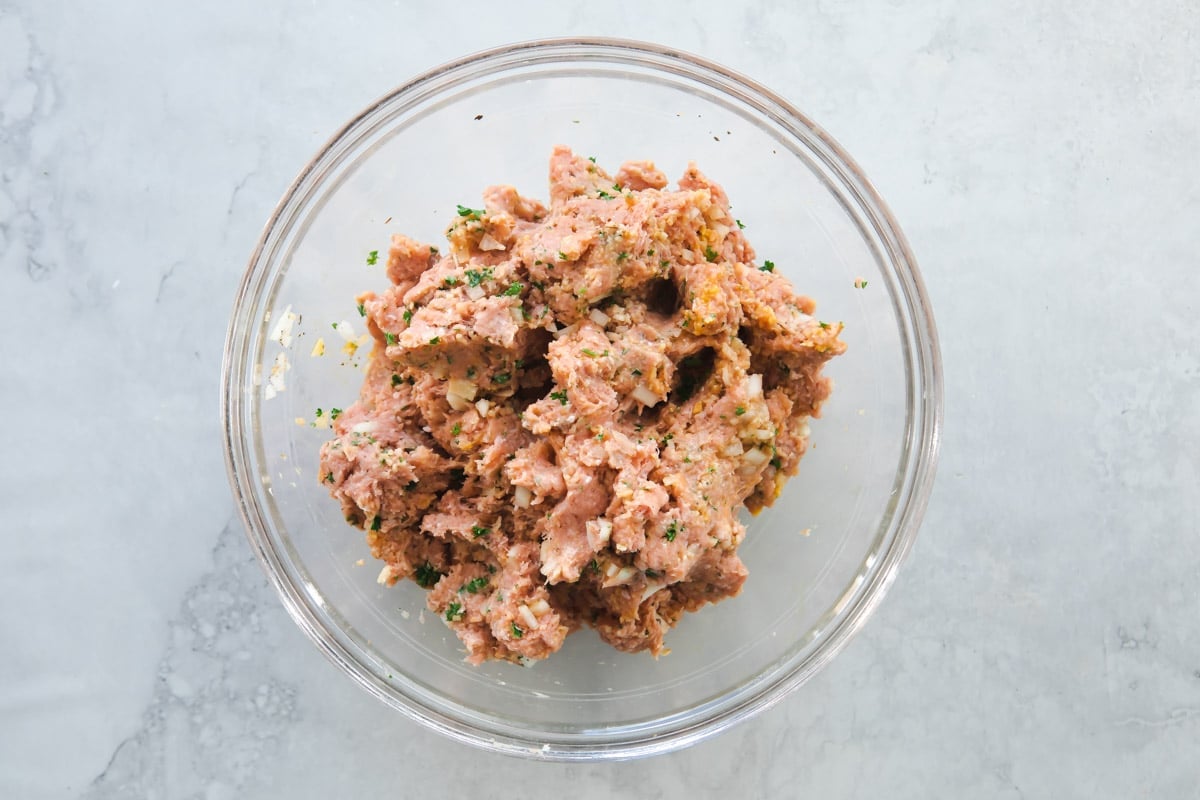 Ingredients for meatballs mixed in a clear glass bowl.