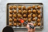 Rows of baked meatballs on a baking rack set over a baking sheet.