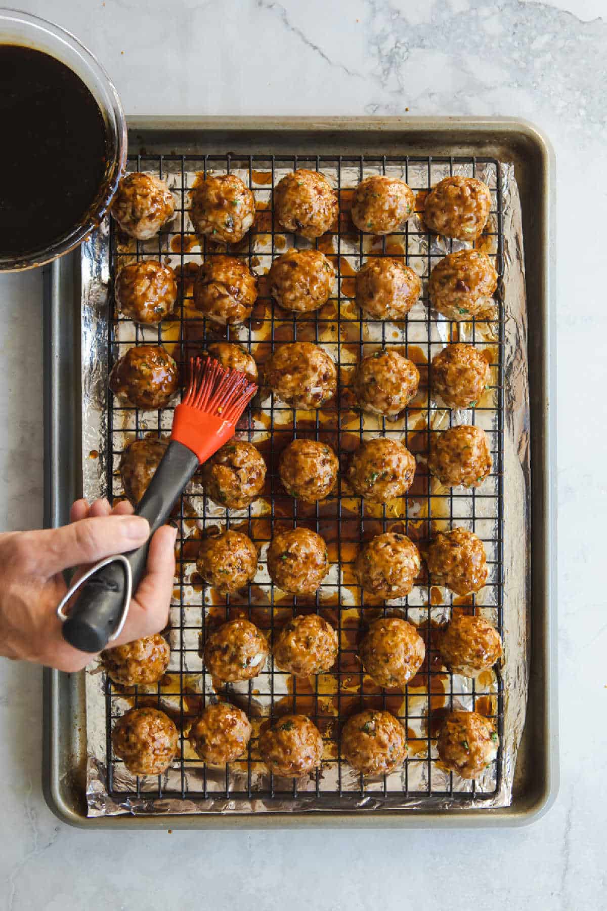 Rows of baked meatballs on a baking rack set over a baking sheet.