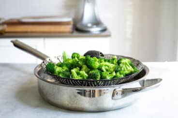 A steam basket full of broccoli in a saucepan.