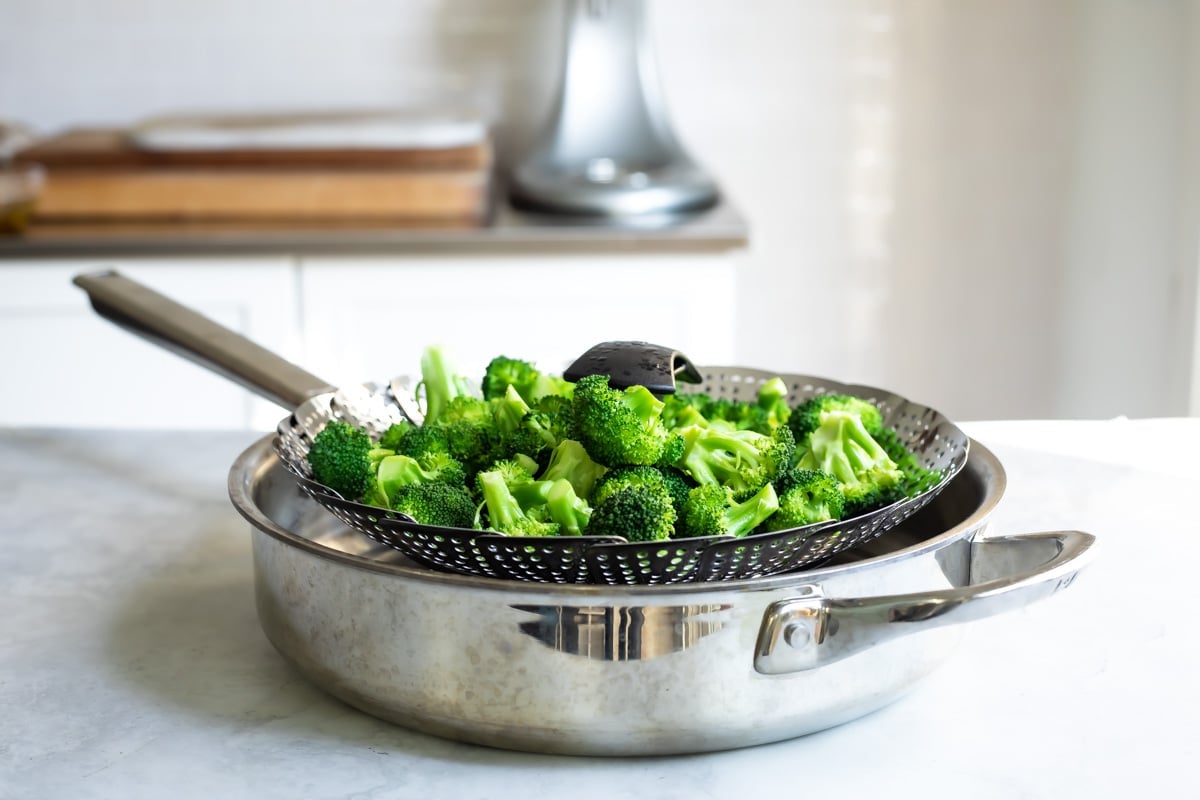 A steam basket full of broccoli in a saucepan.