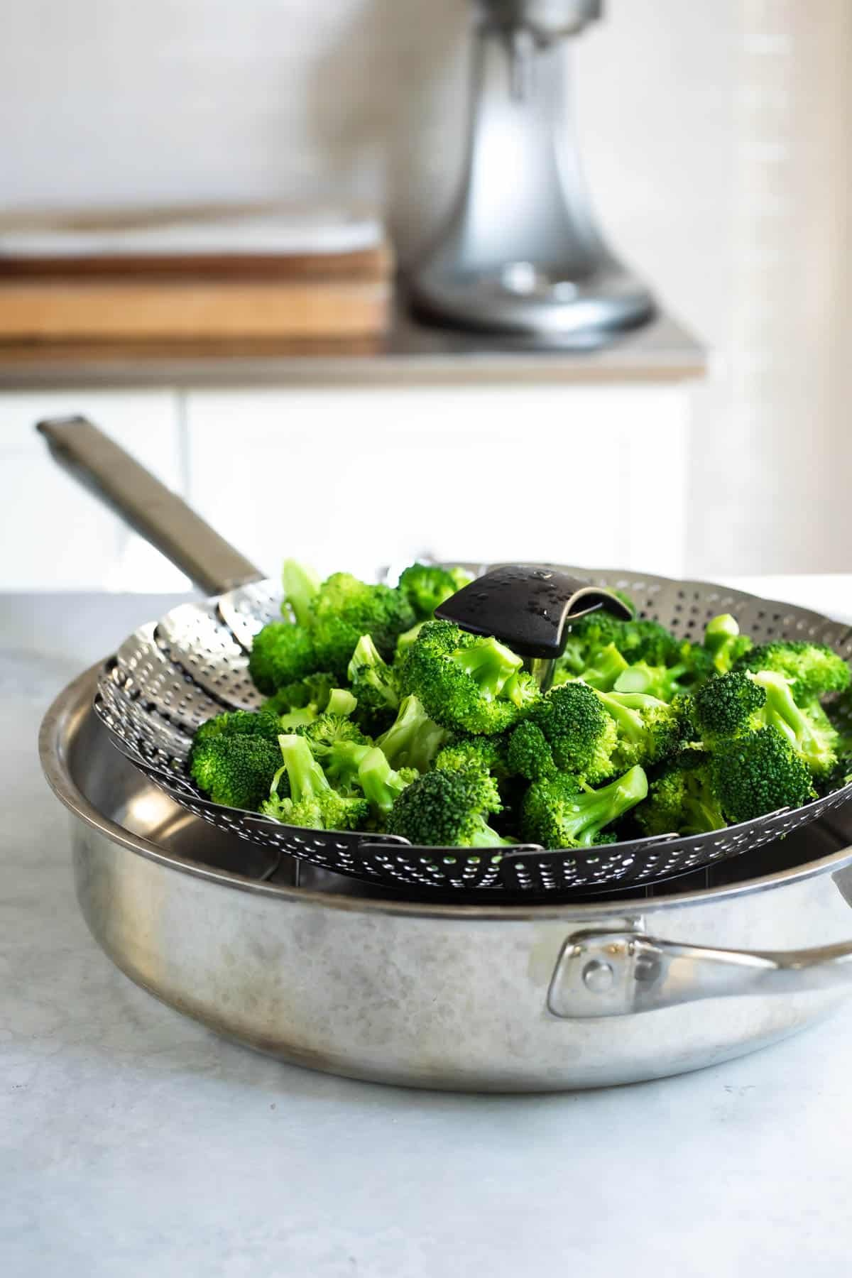 A steam basket full of broccoli in a saucepan.