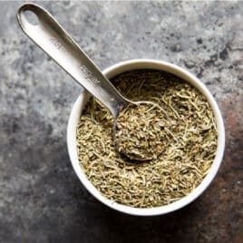 A small bowl filled with Italian seasoning and a measuring spoon.