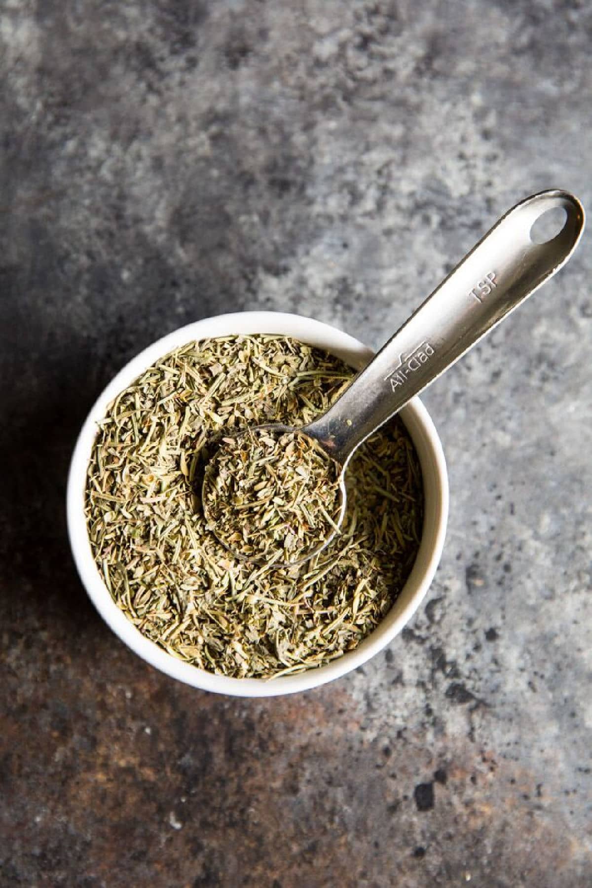 A small bowl filled with Italian seasoning and a measuring spoon.