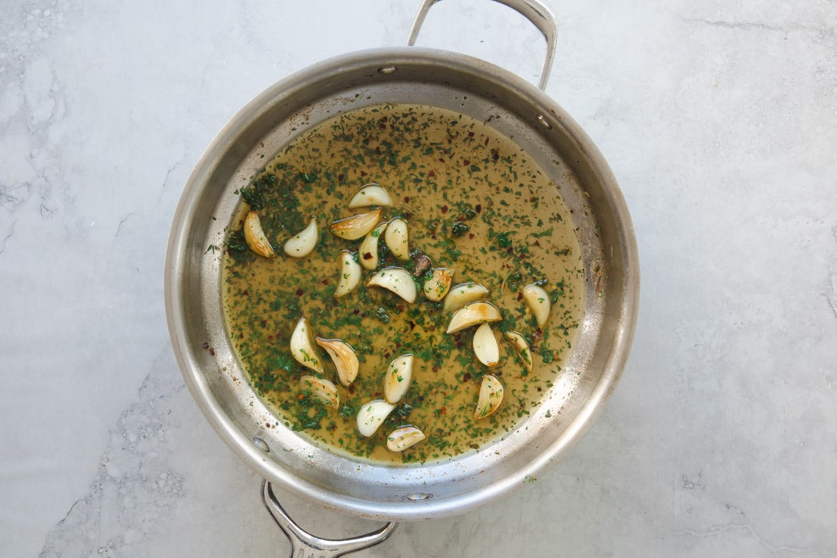 Garlic and herbs cooking in wine in a skillet.