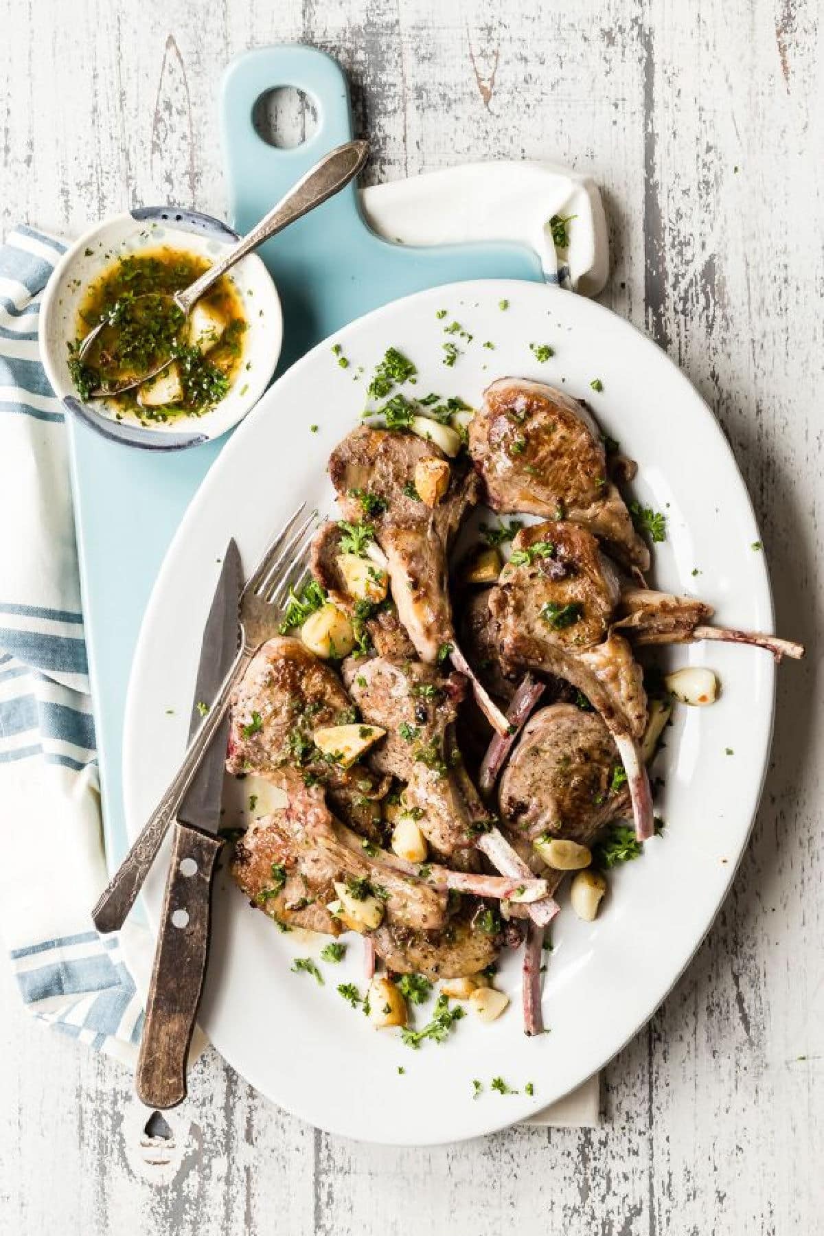 A white platter full of lamb chops garnished with garlic.