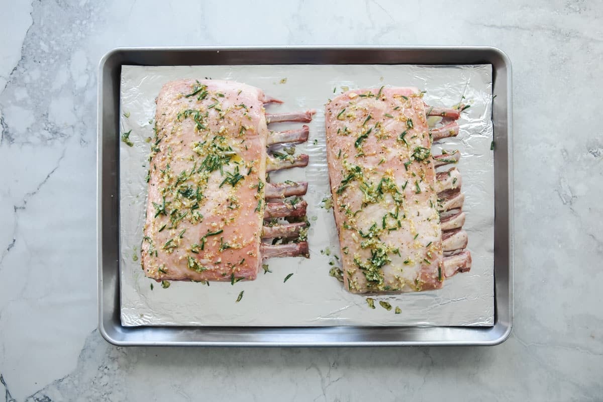2 raw racks of lamb on a baking sheet.