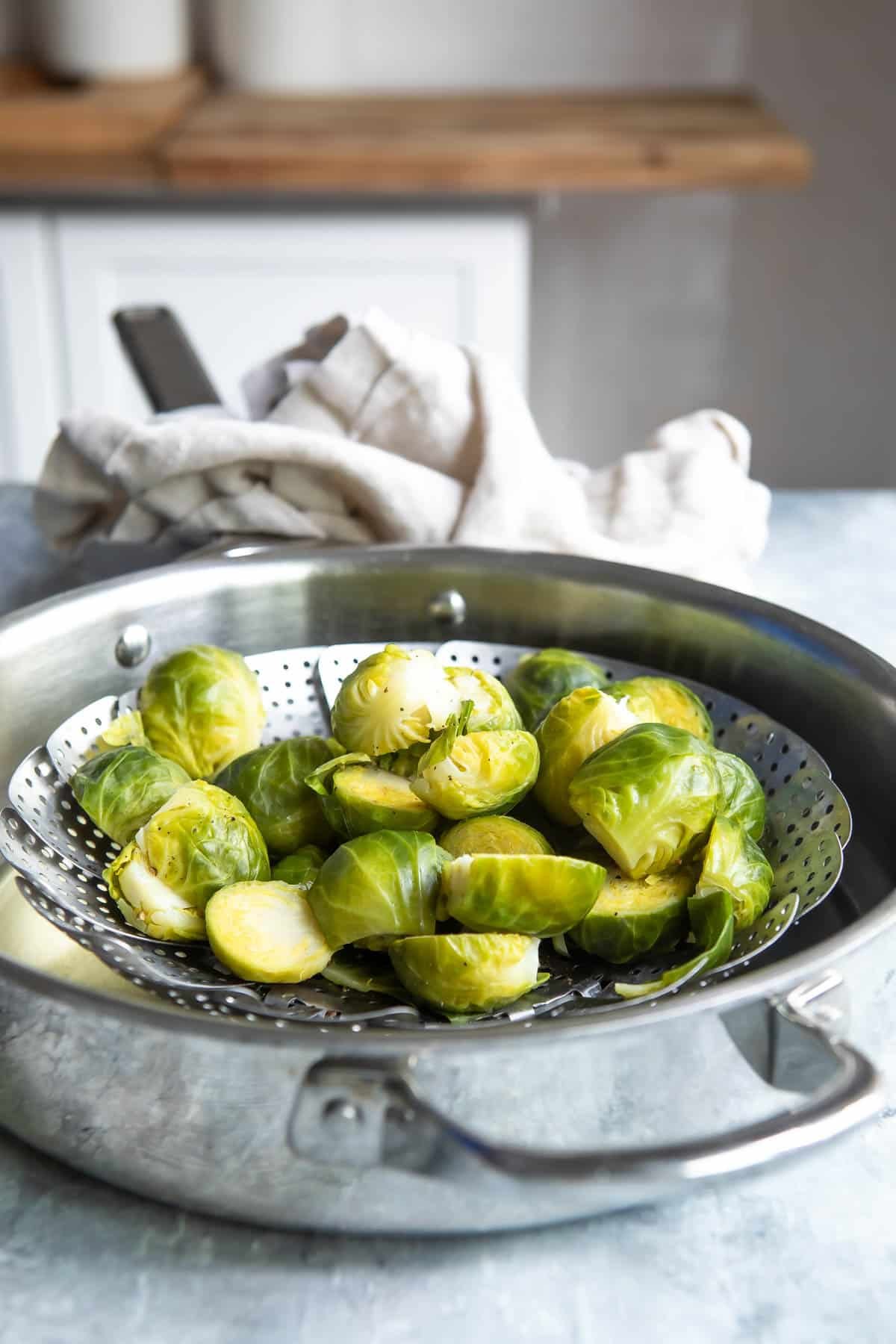 Brussels sprouts in a steamer basket that is resting inside a metal pan.