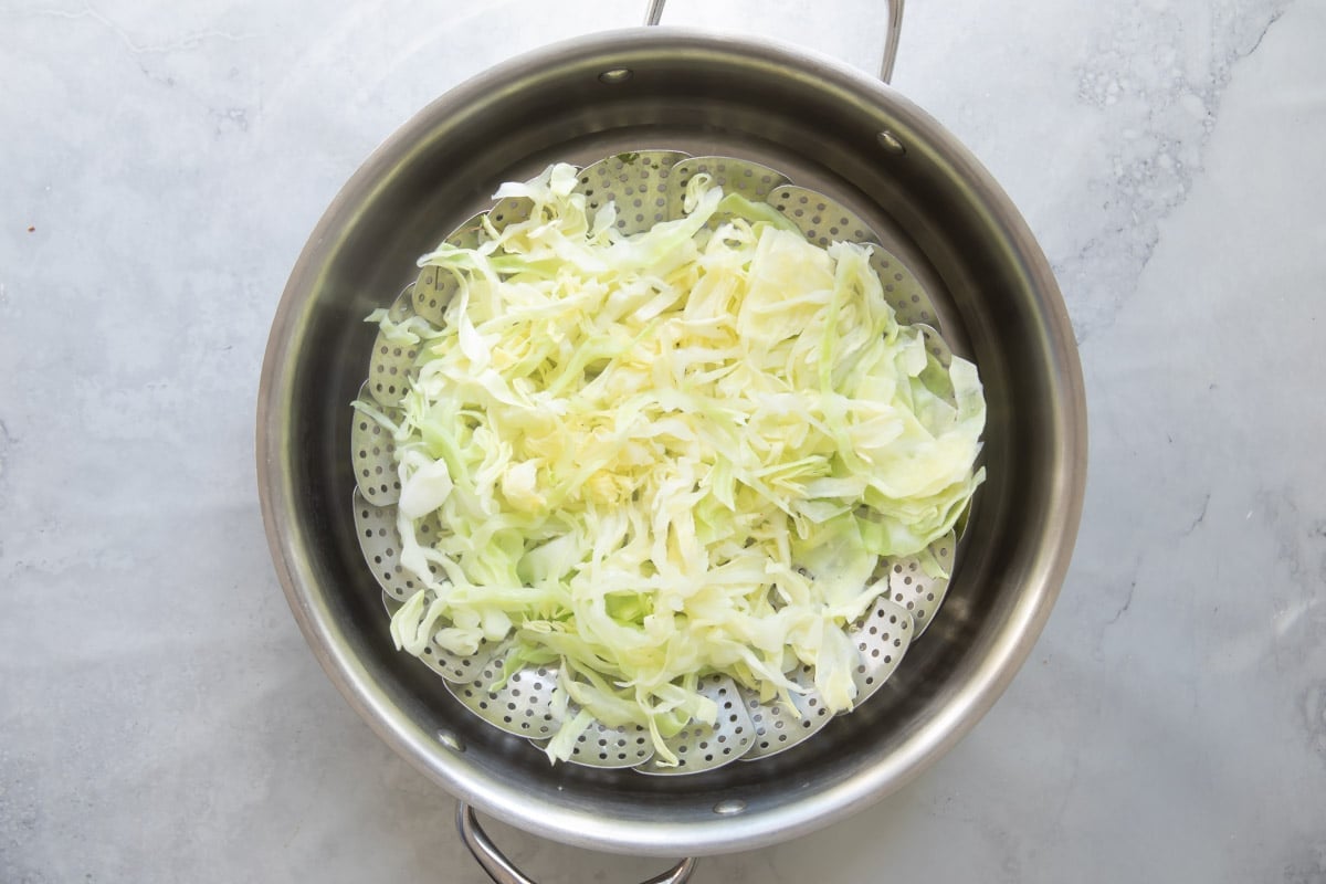 Cabbage while being steamed in a steamer basket in a silver pan.